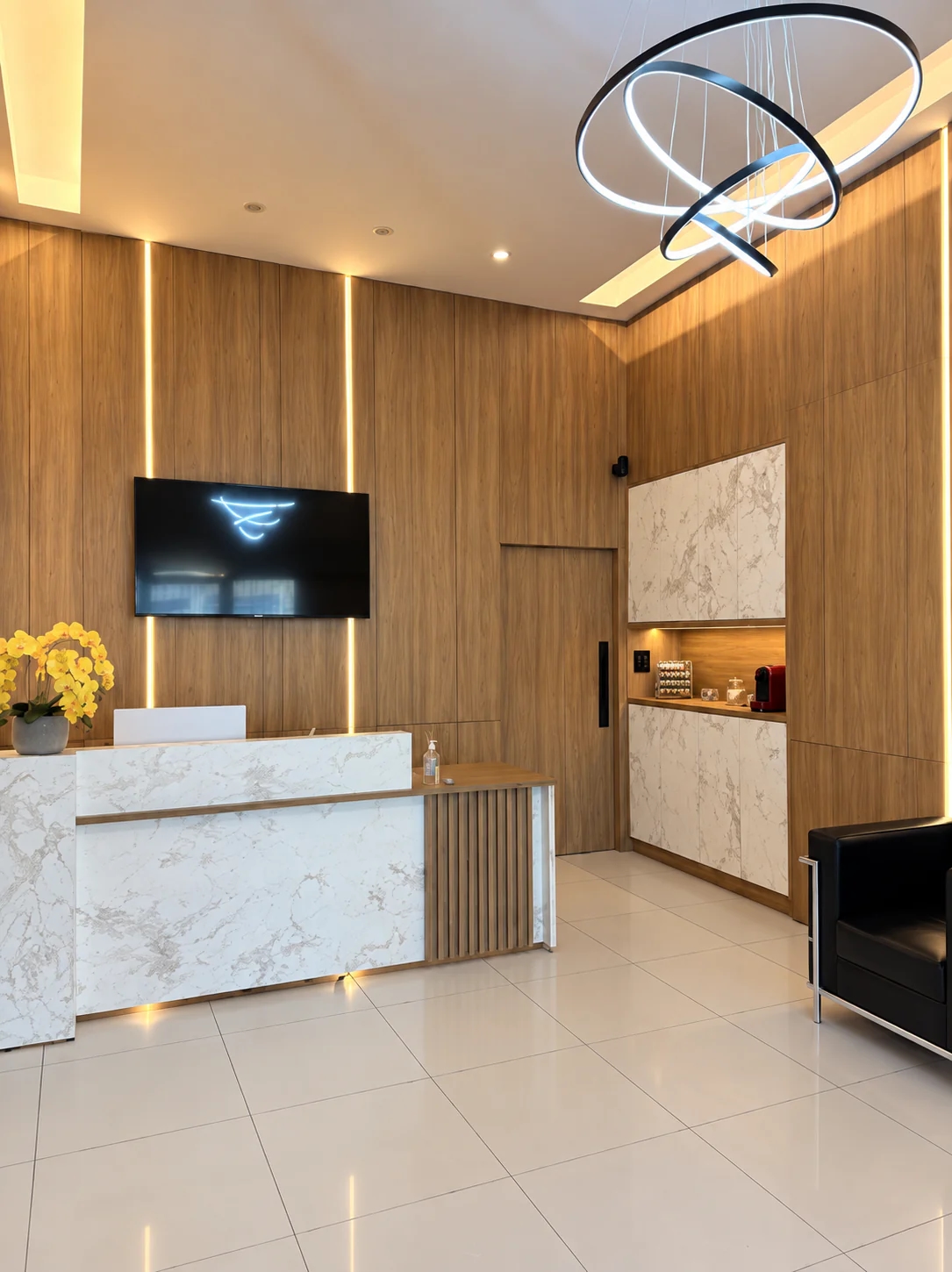 Balcão de mármore branco na recepção da Rodriguez Contabilidade, com painel de madeira ripada, TV e luminária de anéis